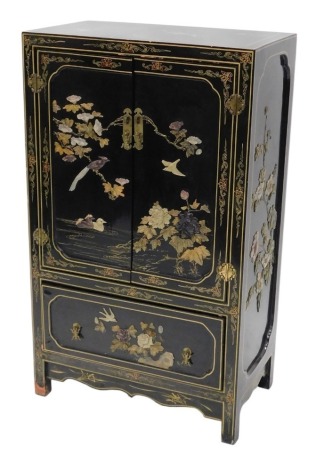 An oriental black lacquered cabinet, with soapstone and mother of pearl Shiboyama style inlay of birds, flowers, etc., with two doors, above a drawer on styles, with shaped apron, 112cm high, 66cm wide.