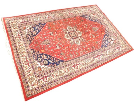 An Indian Mesche carpet, decorated with multicoloured scrolls, leaves, etc., on a red ground, with blue spandrels, one wide, two narrow borders, 199cm x 310cm.