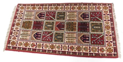 A pair of Indian style rugs, each with a design of square compartments, decorated with leaves, geometric devices, arches, etc., one wide, two narrow borders, 140cm x 71cm, and another of a similar size.