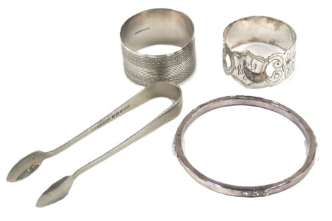 A small group of silverwares, comprising two silver napkin rings, 1.04oz, a costume jewellery bangle, and a set of sugar tongs, stamped Venetian silver. (4)