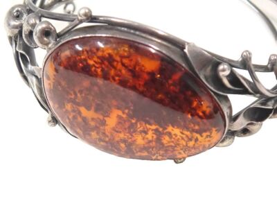 A Danish amber brooch, the oval amber in rub over setting, with vine and lotus flower shoulders, white metal stamped 925, maker JP?, 7cm diameter, 35.3g all in. - 2