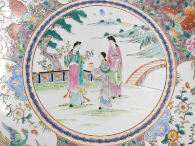 A 20thC Chinese porcelain charger, decorated in coloured enamels, having figures in the central landscape and enclosed by a deep border of butterflies, peonies, fruit and birds, marked with an impressed two character seal highlighted in underglaze red, 46 - 2