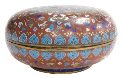 A 19thC Chinese circular compressed cloisonne enamel box, decorated with emblems of flowers and precious objects, on a red ground, the cover with central panel of butterflies and flower heads in polychrome enamels, on a blue ground, 11cm high, 24cm diamet