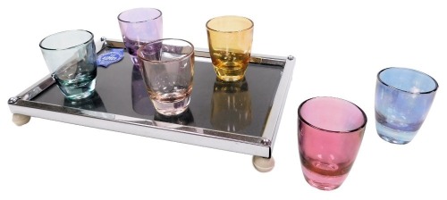 A mid century Zimco glass and chrome liqueur set, with six vary coloured tots, and a rectangular chrome and glass tray, raised on four white Bakelite feet, boxed.