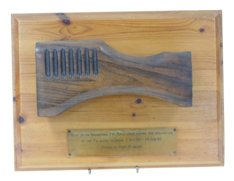 A walnut gun stock, on a pine mount, bearing plaque, Butt of an Argentine FN Rifle Used During the Occupation of the Falkland Islands 2nd April 82, 14 June 82 Found in Port Stanley, the mount 26cm x 35cm.