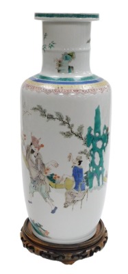 A Qing Dynasty Chinese porcelain famille verte rouleau vase, in Kangxi style, painted with figures in an interior at a games table watching dancers in a garden, 19thC, 49cm high, with associated circular wooden stand.