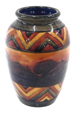 A William Moorcroft Dawn pattern ovoid vase, decorated with a band of trees against a red and orange sky, within two chevron bands, impressed marks and signature to underside, 24cm high.