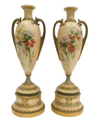 A pair of Royal Worcester blush ivory ground two handled vases, painted with flowers, on a tapering stem and domed foot, printed marks in puce to underside, registration number 304838 above 1957, 27cm high.