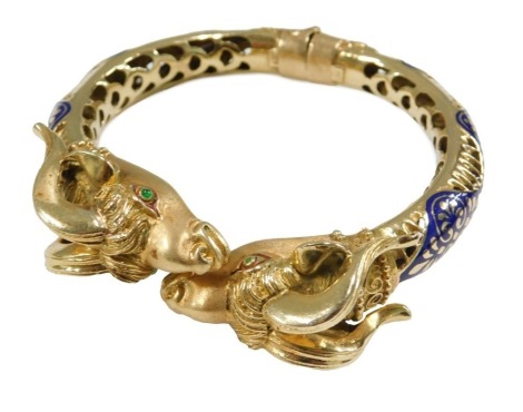 A gold and champleve enamel bangle, with ram's head terminals, the eyes set with cabochon emeralds, with a hinged mechanism, stamped 750, 59.3g.