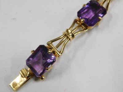 An amethyst seven stone bracelet, in yellow metal, the stone interspersed with tied bows, on a snap clasp, unmarked, 16.8g. - 2