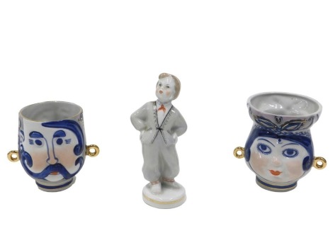 A Russian Riga porcelain figure of a boy and two Kiev USSR cups, each decorated with a face. (3)