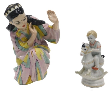 A Ukraine porcelain figure of a seated lady, wearing a pink, pale blue and yellow dress, printed marks in blue to underside, 23cm high, and a Ukraine porcelain figure of a child riding a rocking horse, 6cm high.