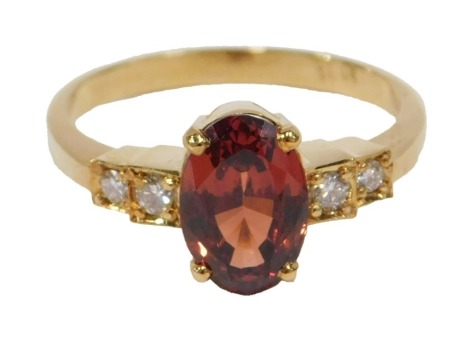 A 20thC garnet and diamond five stone dress ring, with central oval cut orange/brown garnet, 9.8mm x 6.7mm x 5.15mm, approx 2.88ct, flanked by two round brilliant cut diamonds to each side, of graduating size from 0.03ct - 0.02ct, yellow metal stamped 18c