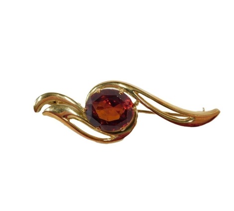 A single stone garnet set bar brooch, the oval cut garnet, 13.7mm x 11.45mm x 7.38mm, approx 10.11ct, in a scroll design outer setting, yellow metal stamped 18ct, 5cm wide, 10.6g all in.