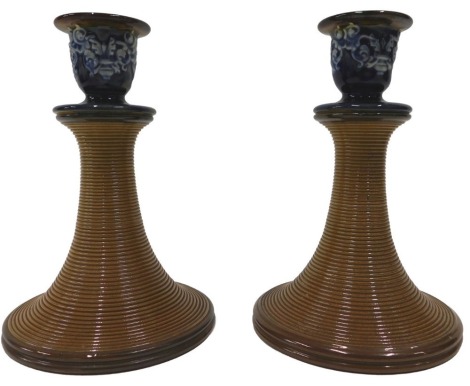 A pair of Doulton Lambeth stoneware candlesticks, with brown and blue glazed sconce, ribbed tapering stem, and impressed marks to underside, 17cm high.