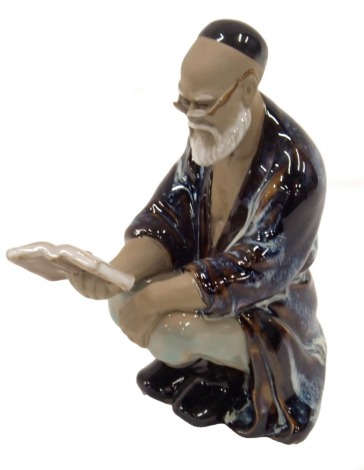 A Chinese porcelain figure of a gentleman seated reading a book, mottled blue, brown and white glaze, 14cm high.