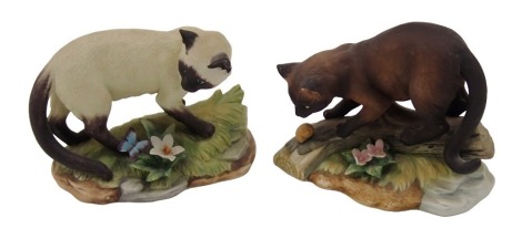 A Kowa porcelain Siamese cat, standing on grass beside a flower and butterfly, and a similar Burmese cat. (2)