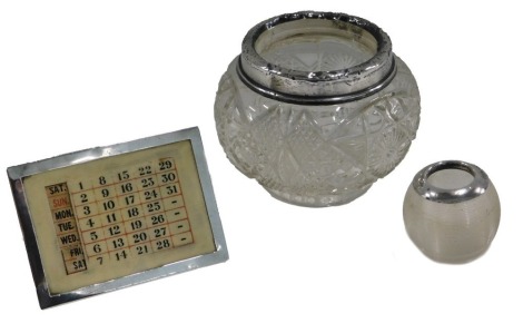 A silver mounted ivorine desk calendar, a cut glass hair tidy with silver rim, a match strike with silver collar. (3)