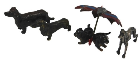 A collection of dog ornaments, to include a cold painted group of two Dachshund puppies and an umbrella, a silver coloured metal Greyhound, and two further Dachshunds. (4)