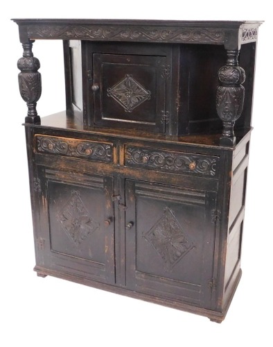 A carved oak court cupboard, the top with a panelled door, decorated with lozenge, on cup and cover supports, the base with two drawers and two doors, on styles, 150cm high, 120cm wide.