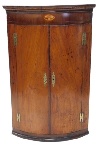 A 19thC mahogany bow fronted corner cabinet, with a chequer banded frieze inlaid with a marquetry bee, above two doors each with brass H hinges, 113cm high, 72cm wide.