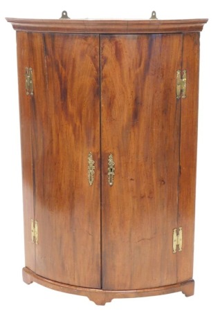 A 19thC mahogany bow fronted corner cabinet, with a moulded frieze above two doors enclosing later black painted interior, with brass H hinges, on bracket feet, 107cm high, 73cm wide.