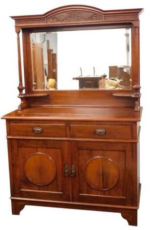 An early 20thC walnut sideboard, the raised top with part carved fluted frieze above a rectangular bevelled plate, on turned supports, the base with a moulded edge and two frieze drawers above two doors with circular panels, on bracket feet, 193cm high, 1