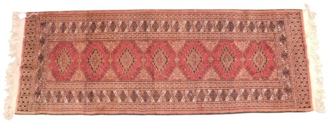 An Afghan style runner, with a design of red lozenges, on a coral ground with one wide and two narrow borders.