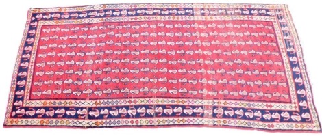 An Afghan red ground rug, decorated with centrally with repeat decoration within one wide and two narrow borders, 267cm x 123cm.