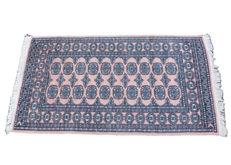 An Afghan style rug, with a design of medallions, on a coral ground, one wide and two narrow borders.