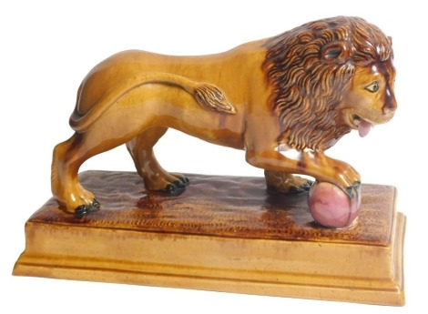 An early 19thC brown glazed Staffordshire lion, after Ralph Wood, with the front right paw resting on a magenta coloured ball, on a rectangular base, 33cm long.