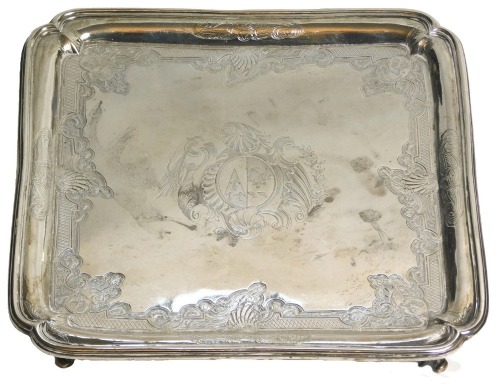 A George II silver square salver, engraved centrally with a crest and overall with an elaborate design of scrolls, shells, leaves, etc., each corner containing a heraldic lion, with re-entrant corners and shaped feet, London 1749, maker William Peaston, 2