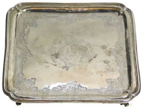 A George II silver square salver, engraved centrally with a crest and overall with an elaborate design of scrolls, shells, leaves, etc., each corner containing a heraldic lion, with re-entrant corners and shaped feet, London 1749, maker William Peaston, 2