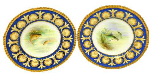 A pair of early 20thC Wedgwood porcelain plates, painted by A Holland, with bream, and carp, within a powder blue and gilt floral border, pattern number W1947, painted and printed marks, 23cm wide.