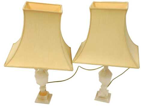 A pair of alabaster table lamps, with foliate scroll handles, raised on a stepped square base, with cream coloured shades, 64cm high.