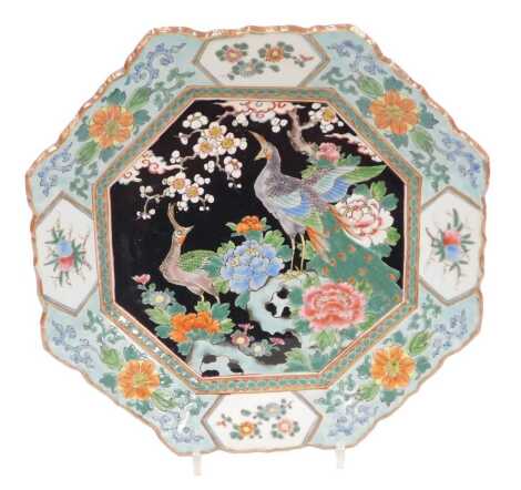 A 19th/20thC Japanese porcelain octagonal plate, the famille noire central panel decorated with peacocks, peonies and apple blossom in coloured enamels, iron red, within wide floral borders signature to base, 33cm diameter.