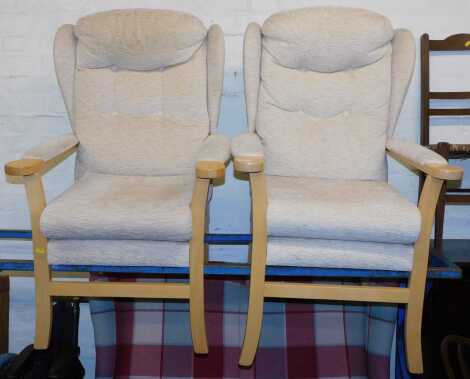 A pair of beech framed wing back armchairs, finished in a cream/beige fabric, 68cm wide x 112cm high x 67cm deep.