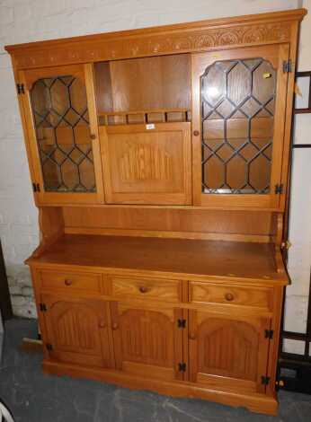 A light oak lounge unit, with high level glazed leaded display cabinets and central drinks cabinet, with drop down leaf, frieze draws and scroll detail to door panels, overall size 134cm wide x 187cm high x 46cm deep.