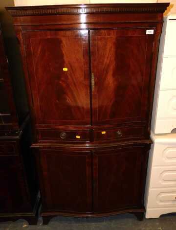 A mahogany serpentine fronted storage unit, with two upper doors, central frieze drawers and two low cupboards, raised on bracket feet, with dental detail and bevelled top, 82cm wide x 155cm high x 44cm deep.