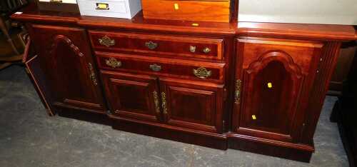 A reproduction teak break front sideboard, with brass escutcheon detail, and carved panel doors, 162cm wide x 77cm high x 45cm deep.