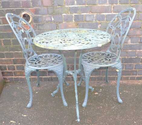 A green painted cast metal garden table, with two chairs.