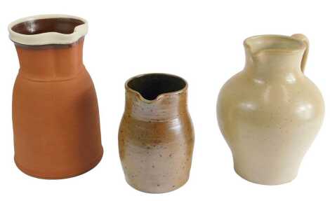 A 19thC buff coloured stoneware jug, 22cm high, a darker stoneware jug, and a terracotta jug with cream lip. (3)