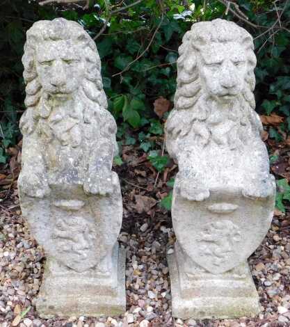 A pair of reconstituted stone heraldic lions, holding a shield, on a square stepped base, 81cm long.