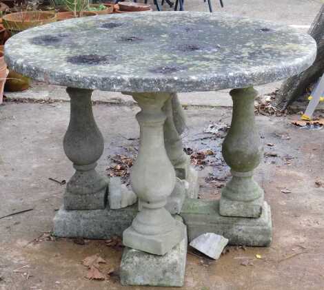 A reconstituted stone garden table, with a circular top, on baluster turned supports and X base.