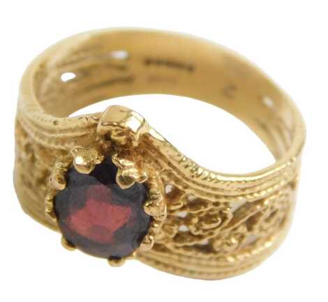 A 9ct gold Eastern inspired dress ring, formed as a wishbone, with pierced scroll decoration and set with oval cut garnet, approximately 0.65ct, maker AJ Ltd, ring size N½, 4.1g.