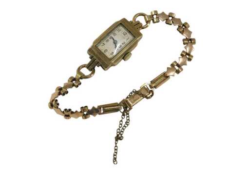 A mid century ladies 9ct gold cased wristwatch, rectangular silver dial bearing Arabic numerals, on a plated strap.