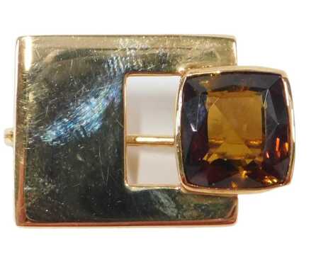 A 20thC andalusite brooch, in modern style, set with a cushion cut brownish red stone, 11mm x 10mm x 6.6mm, approx 5.41ct, in a rub over setting, with a rectangular abstract design bar, on single pin back with pin and revolver, yellow metal believed to be