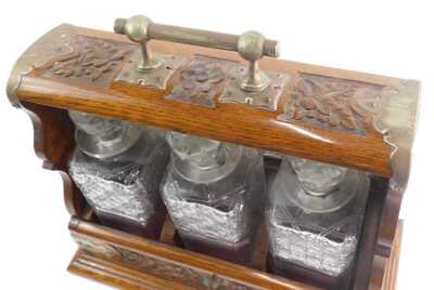 An Edwardian carved oak tantalus, with silver plated mounts, containing three square section cut glass decanters and stoppers, and with mirrored back, 37cm wide. - 2