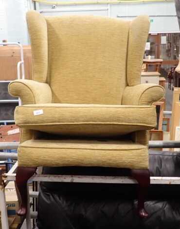 A wingback armchair, in gold coloured upholstery. 
The upholstery in this lot does not comply with the 1988 (Fire & Fire Furnishing) Regulations, unless sold to a known exporter or upholsterer it will be cut from the frame before leaving the premises.