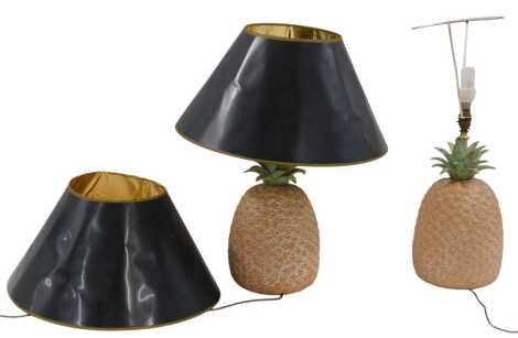 A pair of terracotta lamp bases, each modelled in the form of a pineapple, with brass mounts and black shades, 68cm high overall.